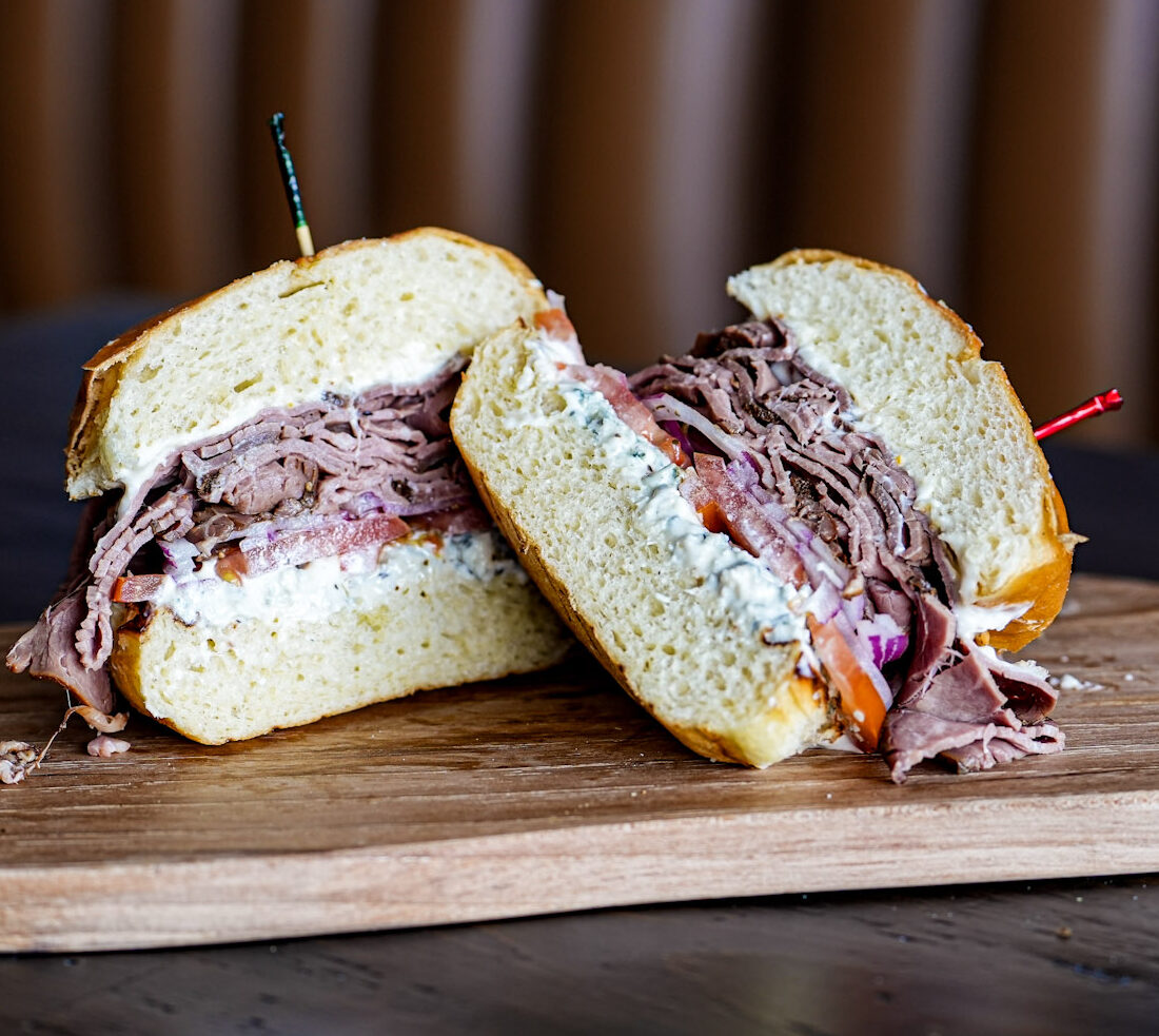 Roast Beef & Blue sandwich on a toasted potato roll with creamed horseradish, tomato and onion